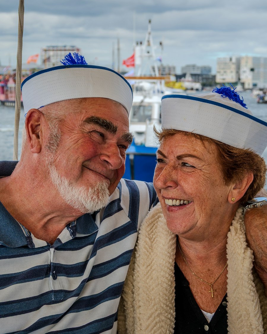 A laughing couple in sailor hats on the deck of a harbor boat