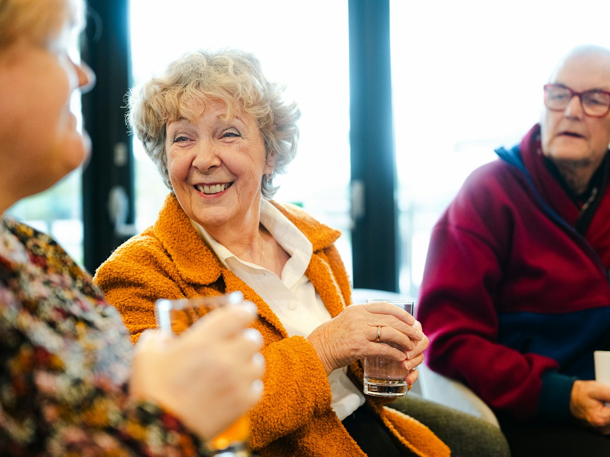 Three friends in their seventies laughing together over drinks